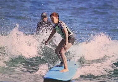 Young surfer riding a small wave on a blue surfboard.